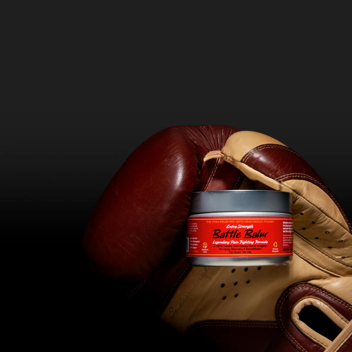 Brown leather boxing glove holding a Battle Balm Extra Strength pro size tin on a dramatic background to show that Battle Balm is a powerful pain reliever used by athletes & pugilists around the world. 
