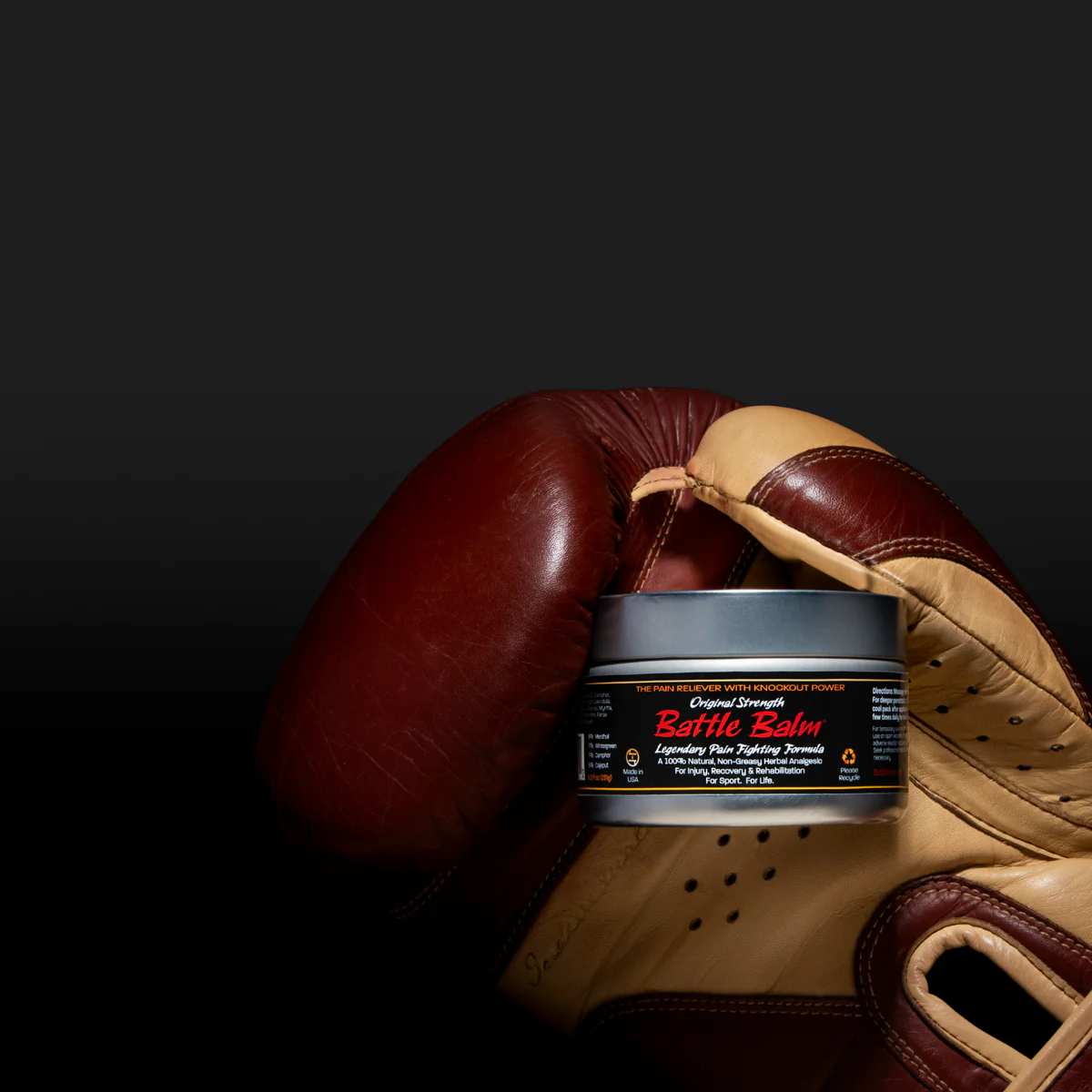 Brown leather boxing glove holding a Battle Balm Original Strength pro size tin on a dramatic background to show that Battle Balm is a powerful pain reliever used by athletes & pugilists around the world. 